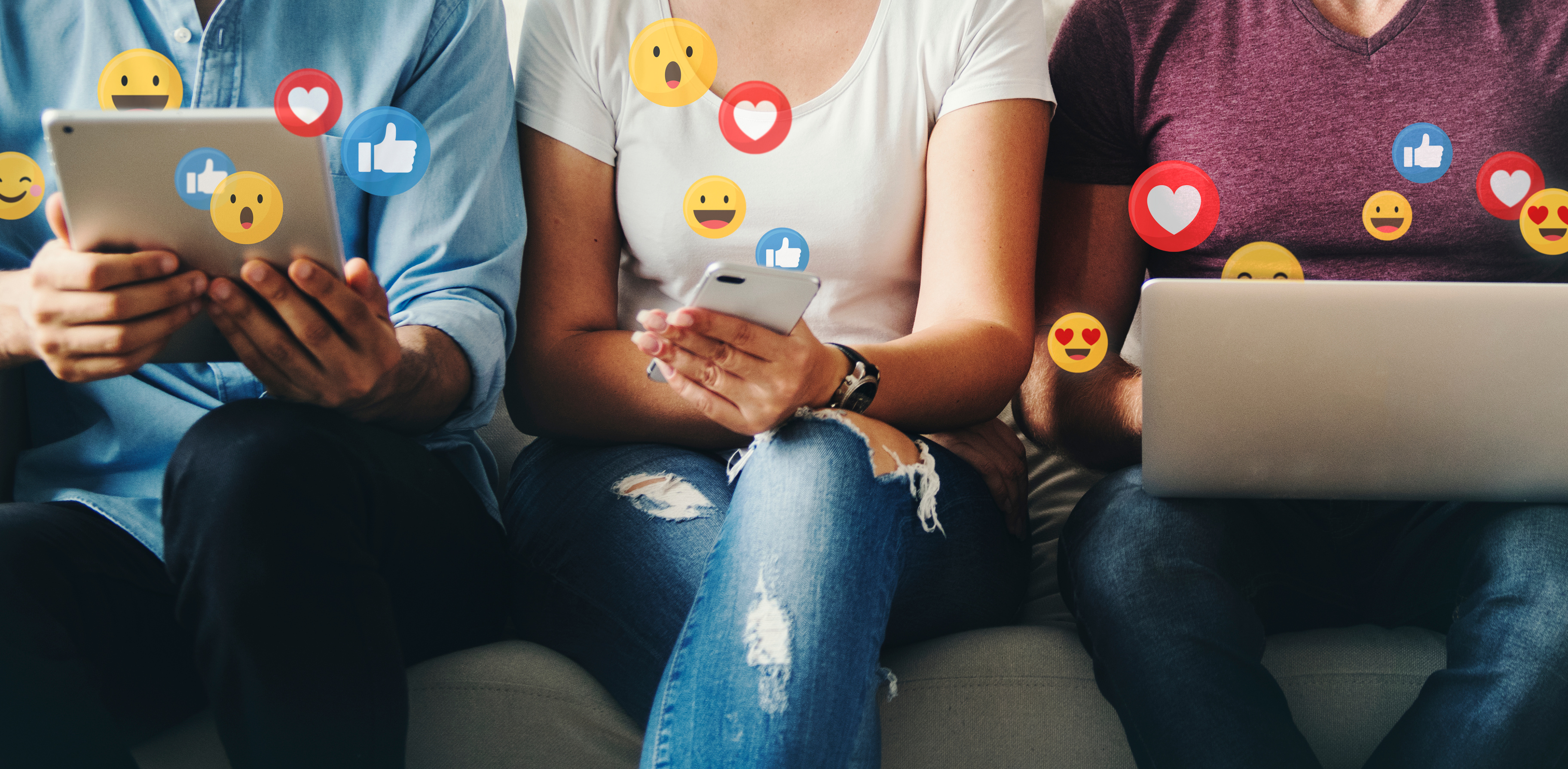 Three individuals sitting on a couch using a tablet, smartphone, and laptop, with social media reaction icons floating around them.