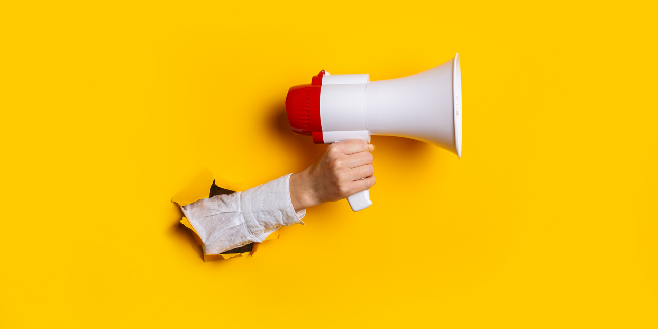 A hand holding a megaphone emerges through a torn yellow paper background.